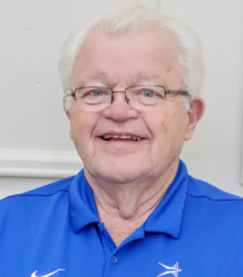 Older man in a blue shirt with grey hair and glasses smiling at the camera